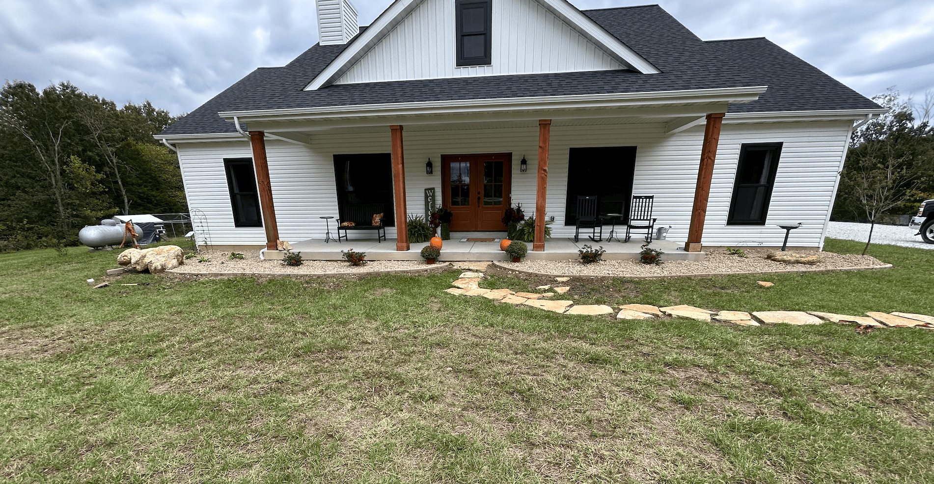 Wide front elevation showing a completed decorative rock bed installed along the full porch frontage