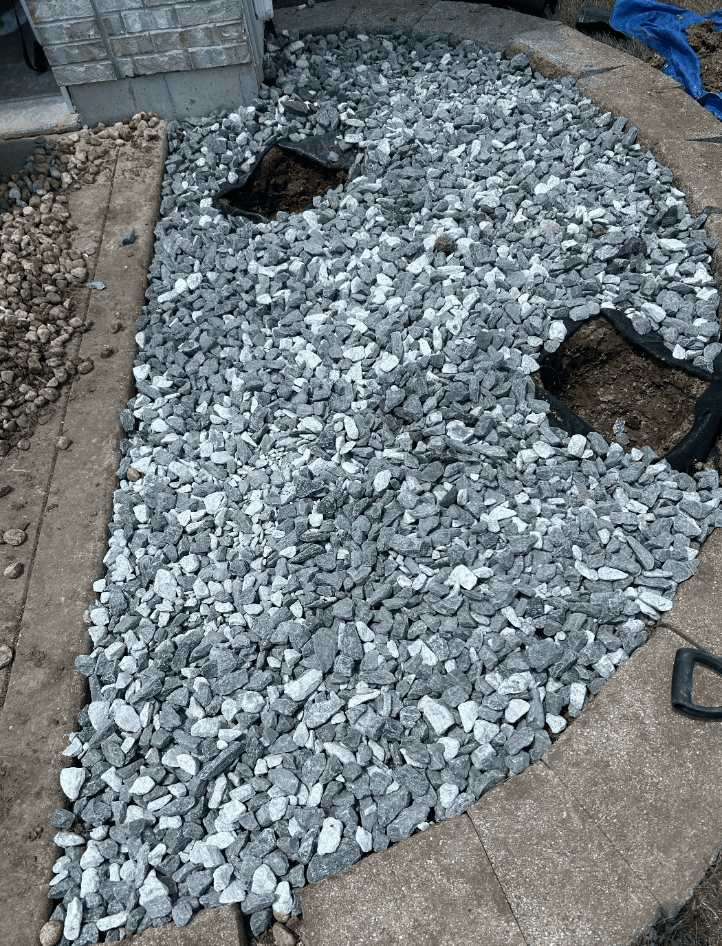 Rounded landscape bed filled with gray decorative rock around two center cutouts