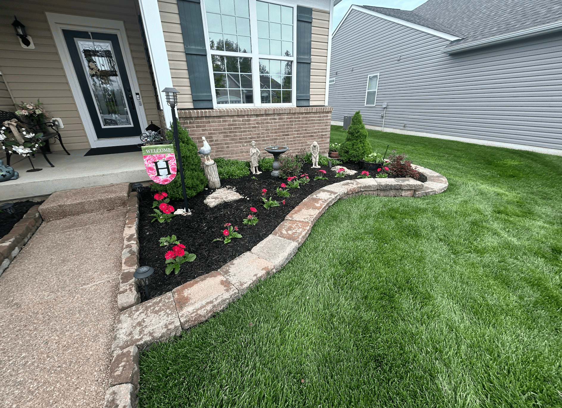 Front entry flower bed with black mulch, stone edging, and new flowers